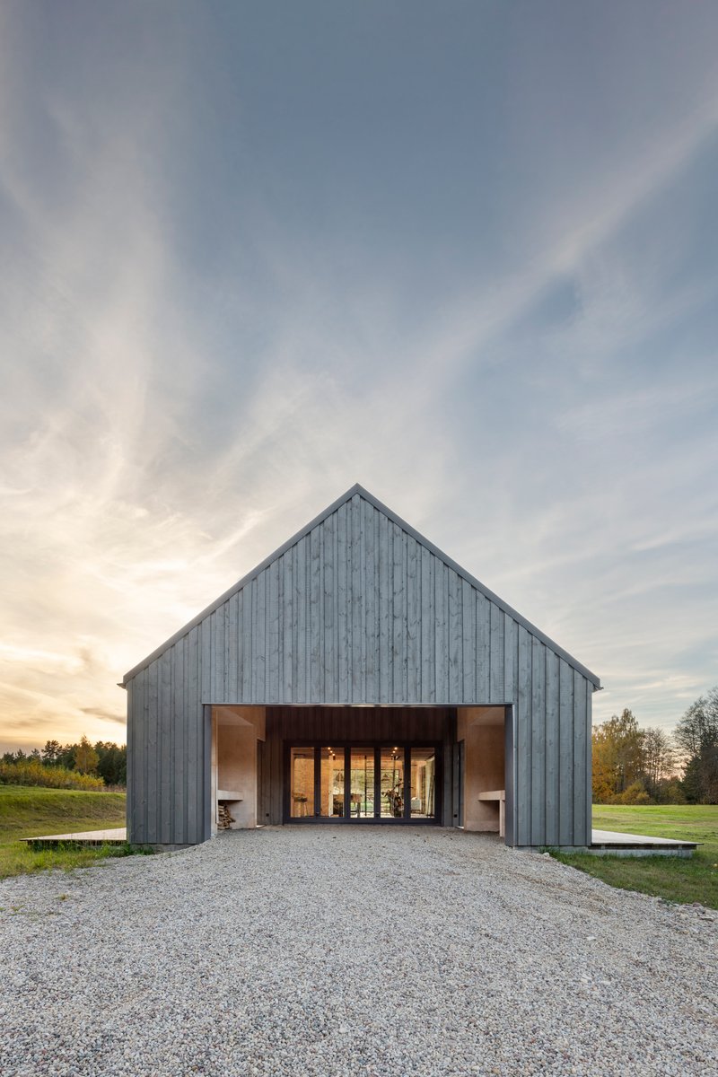 Weathered grey timber facade with a wide central opening facing a gravel approach under a clouded dusk sky