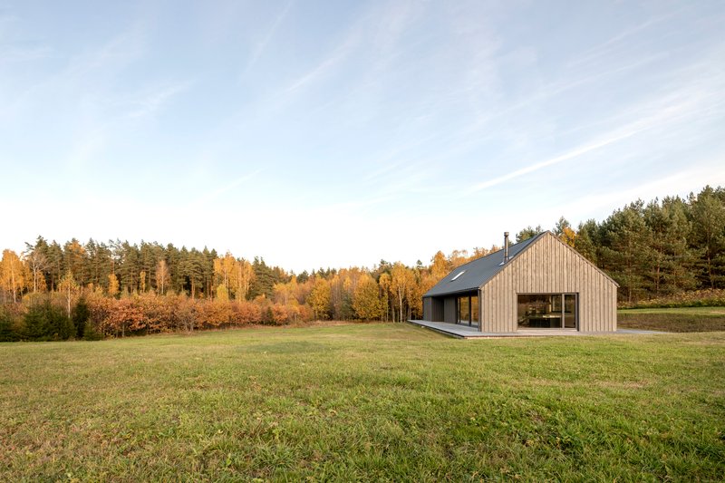 Distant view of the gabled volume in a grass field with forest treeline at golden hour