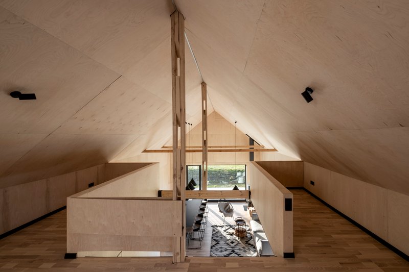 View from the loft level showing the double-height living space with plywood ceilings and timber support beams