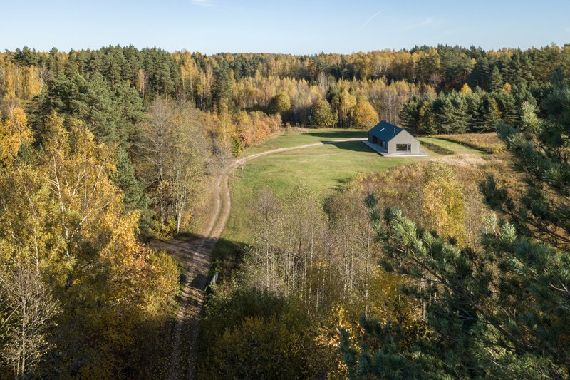 Drone view showing the dwelling positioned in a meadow clearing with winding dirt track