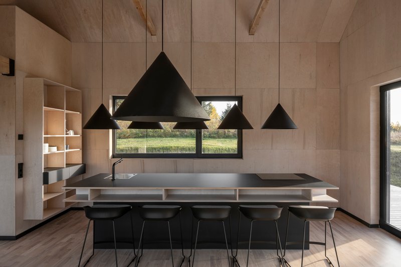 Kitchen island with black metal countertop beneath four triangular pendant lights and horizontal window framing landscape