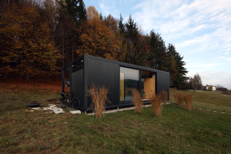 Dark corrugated metal cladding with glazed openings and timber door surrounded by dried grasses