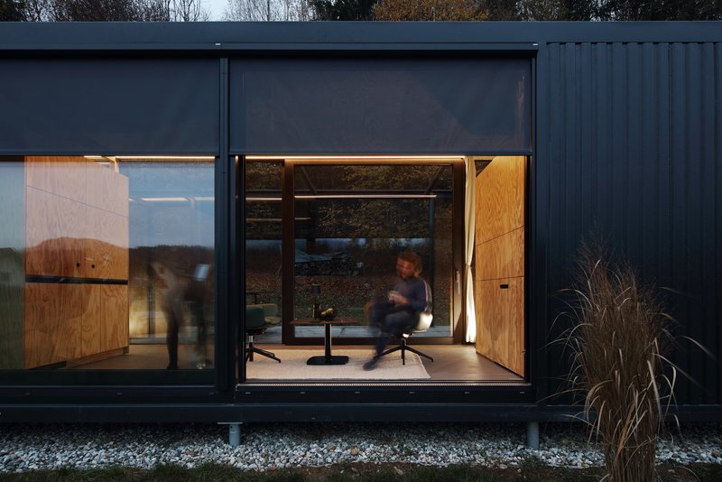 Close view of the glazed facade at twilight with a figure moving through the lit interior