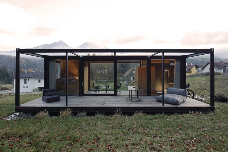 Glass-walled pavilion with black steel frame and covered terrace overlooking a mountain valley at dusk