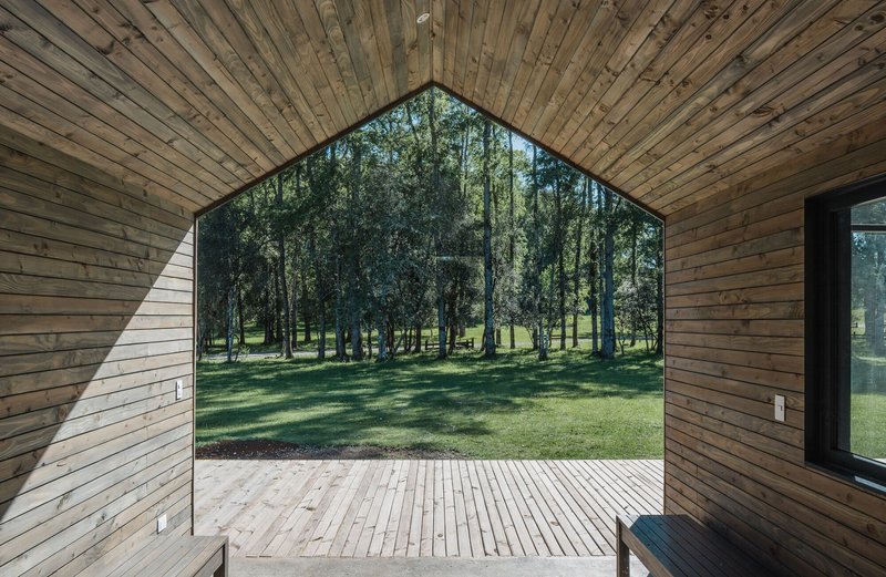 Arched opening with timber cladding and frameless glass revealing a wooden deck and tree grove