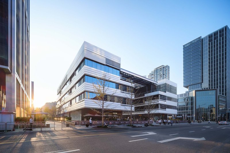 Oblique street view of the horizontal metal louvered facade with planted trees at sunrise