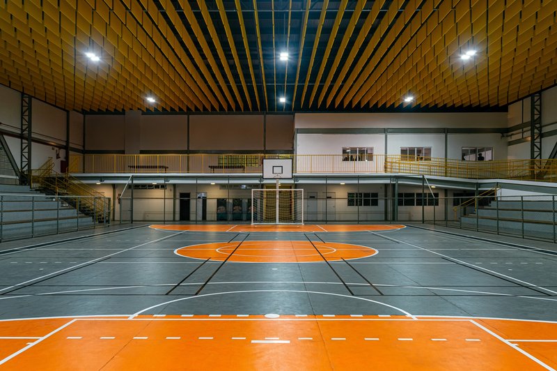 Indoor sports court with orange markings on grey flooring beneath a slatted timber ceiling