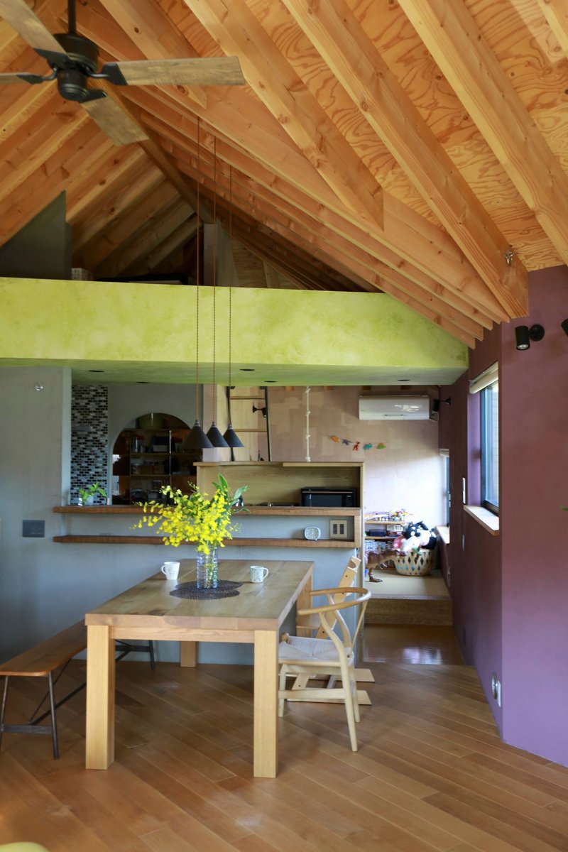 Dining area beneath exposed timber trusses with plywood ceiling and yellow flowers on the table