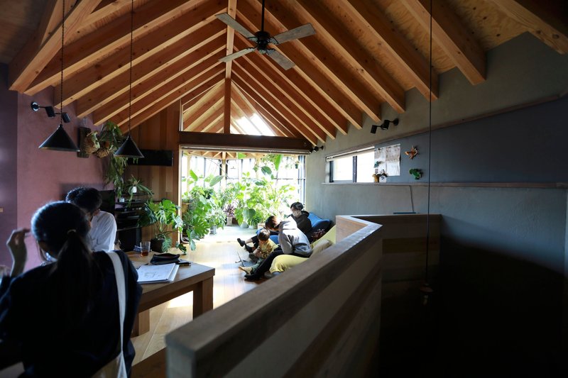 Long view across timber dining table toward inhabitants beneath the vaulted rafter ceiling
