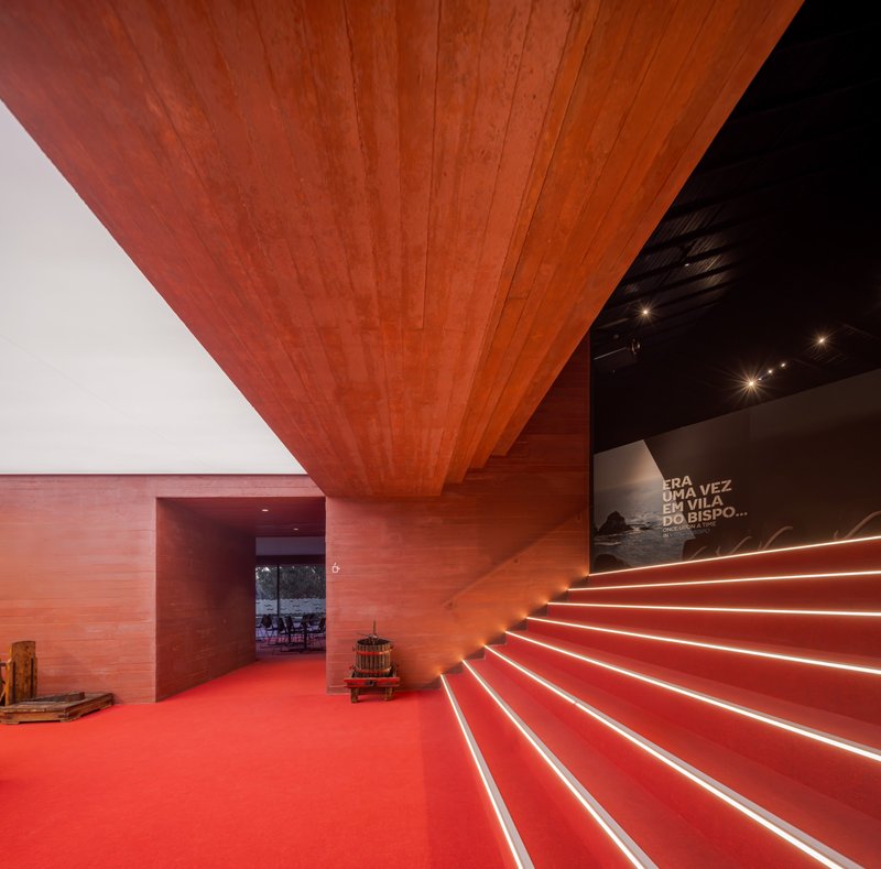 Interior lobby with red tile staircase with embedded linear lighting ascending beneath exposed tile soffit
