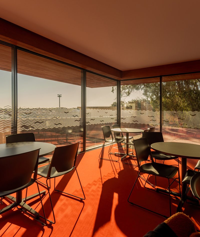 Interior dining space with orange flooring and full-height glazing overlooking a chevron-patterned screen wall