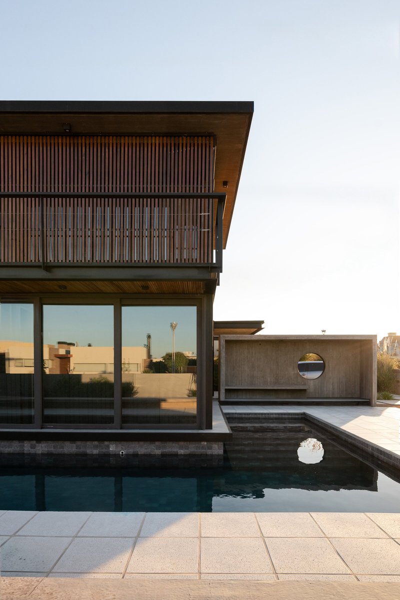 Upper-level terrace with slatted timber screens and cantilever overhang above a pool and circular window volume