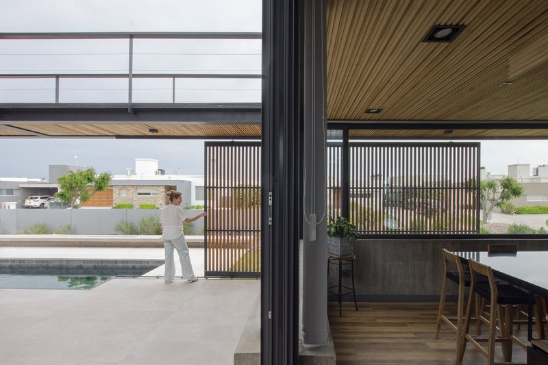 Interior view through sliding doors to pool terrace with timber ceiling and vertical slat screens beyond