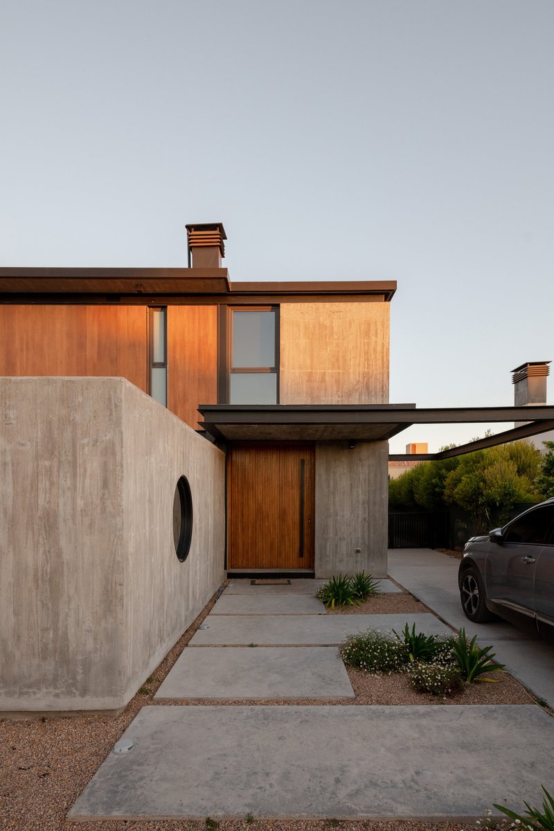 Entry facade with timber panels, concrete wall and circular porthole window at dusk