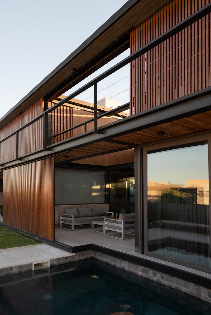Poolside terrace with timber slat screens, black steel columns and slatted wood soffits at dusk