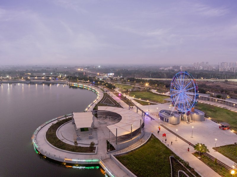Circular pavilion with curved canopy and illuminated ferris wheel beside the waterfront at dusk