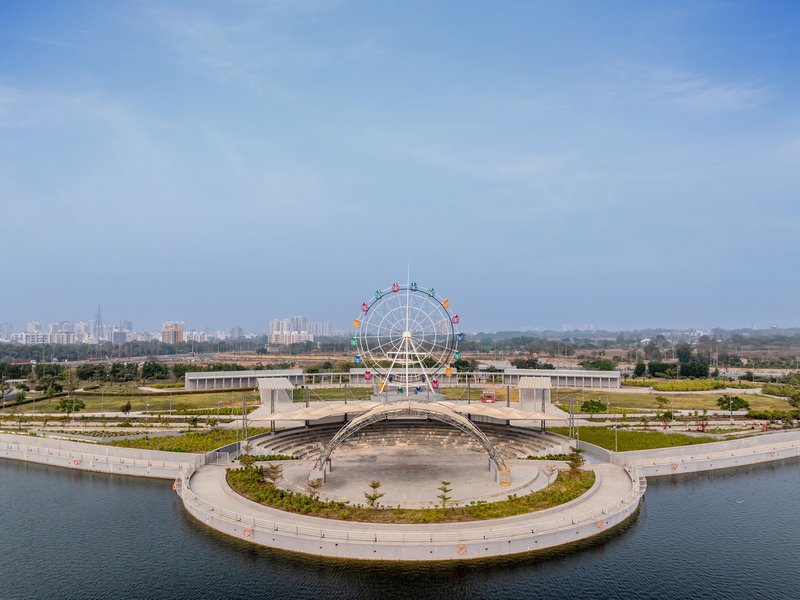 Curved waterfront plaza with a central pavilion and ferris wheel in the distance