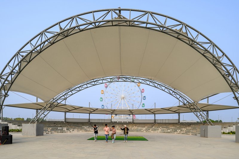 Tensile fabric canopy with exposed steel truss structure framing a distant ferris wheel