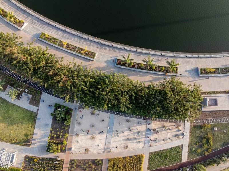 Drone view of the curved waterfront promenade with planted beds and pedestrians along the lake edge
