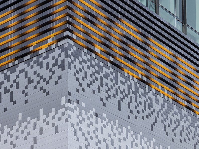 Corner facade with pixelated white panels below horizontal orange and black banded cladding
