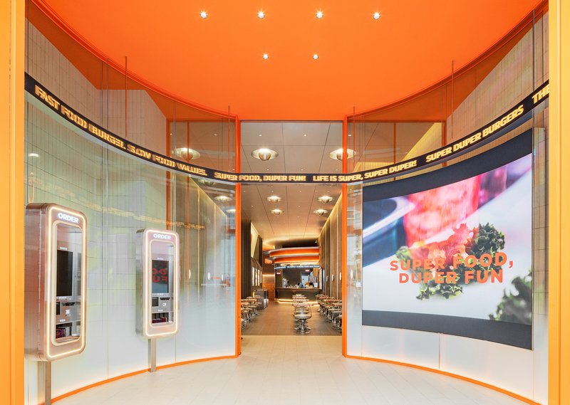 Entry vestibule with orange ceiling, glass walls, ordering kiosks, and view into dining area