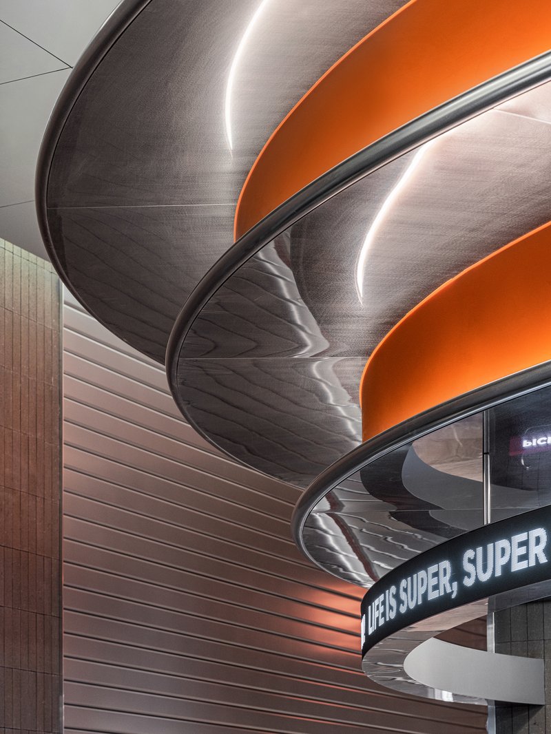 Close-up of layered curved ceiling baffles with orange bands and edge-lit perimeters