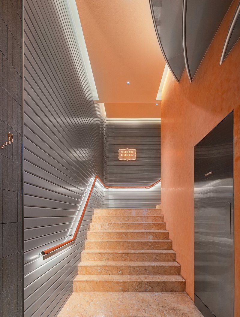 Staircase with ribbed wall panels, orange ceiling, and concealed cove lighting