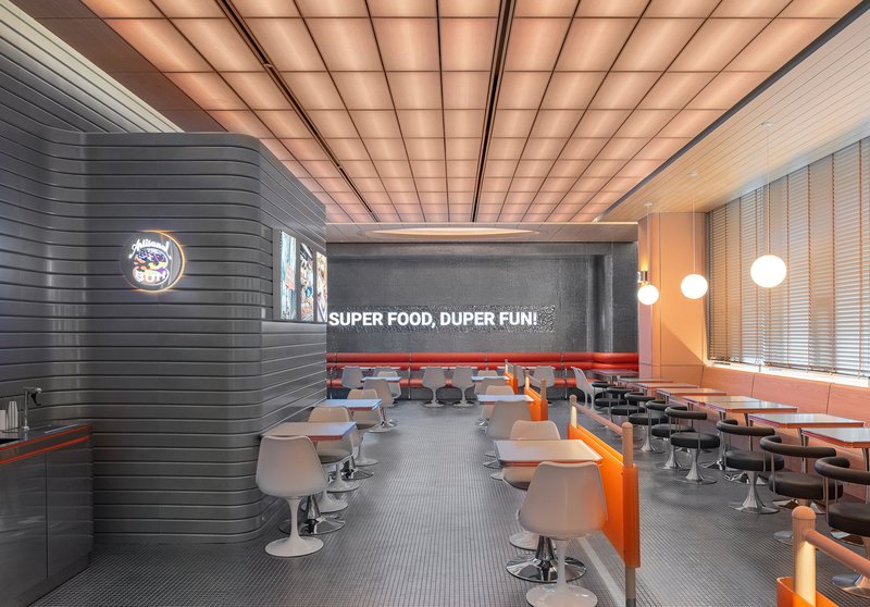 Dining area with horizontal ribbed dark grey wall and rows of pedestal tables under gridded ceiling