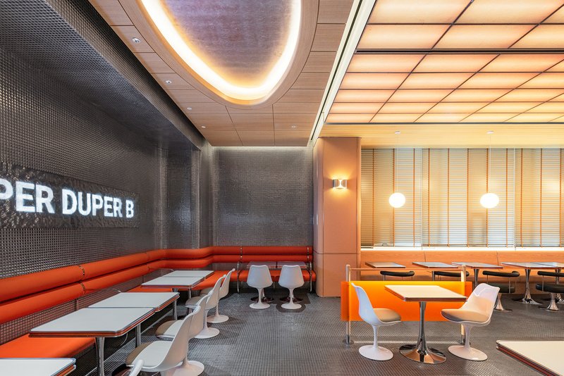 Curved banquette seating upholstered in orange vinyl against dark tiled wall with backlit ceiling cove
