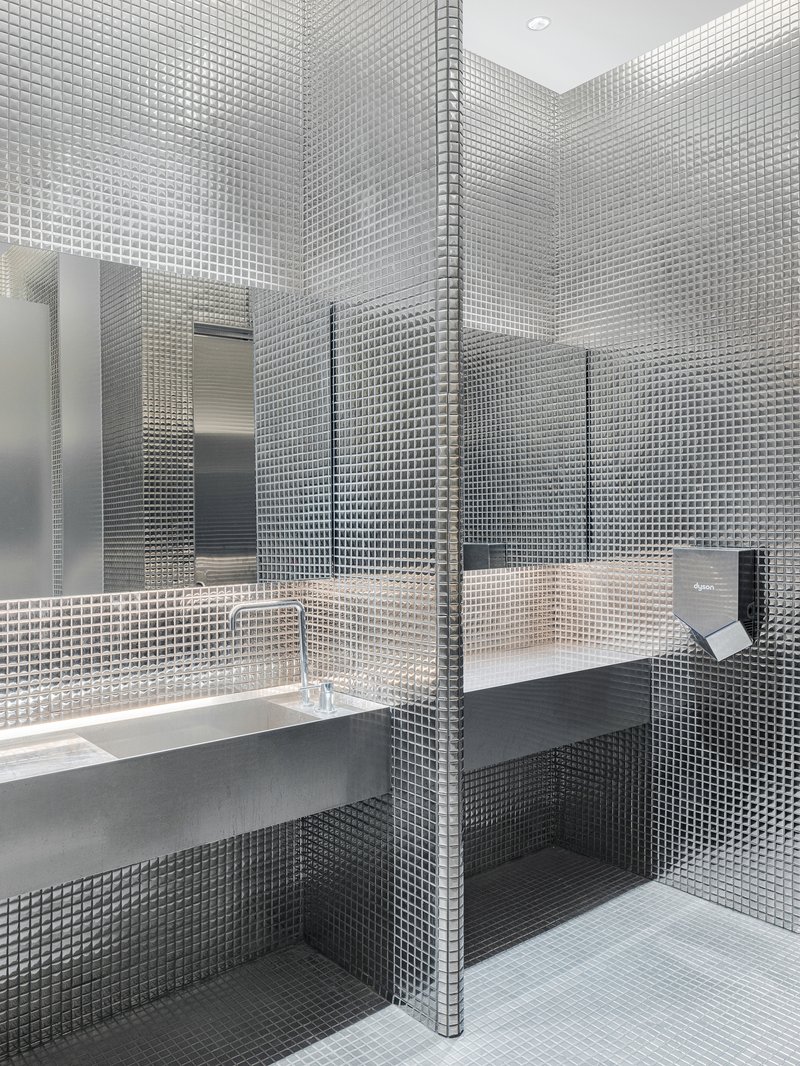 Restroom interior clad in small square mosaic tiles with wall-mounted sink and mirror