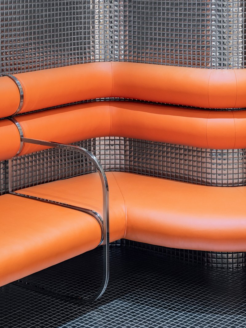 Close-up of orange vinyl booth seating with chrome edge trim against small dark mosaic tile wall