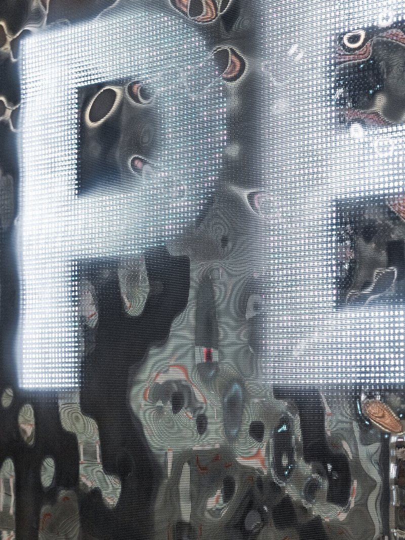 Reflection through perforated metal mesh screen showing distorted silhouette of a figure
