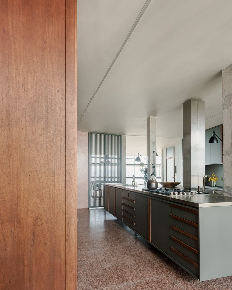 Kitchen with timber cabinetry, stainless steel countertops and fluted glass screening behind concrete columns