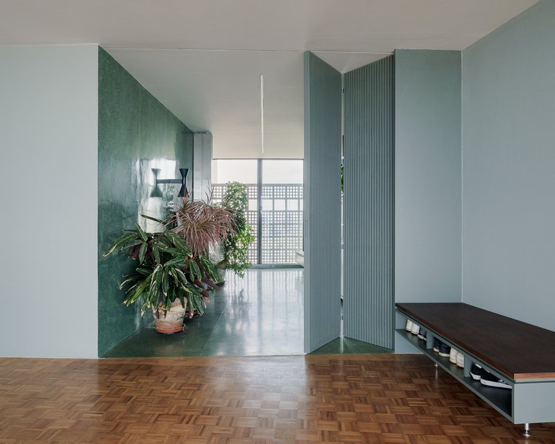 Folding ribbed partition door in blue-green connecting two interior spaces with parquet flooring
