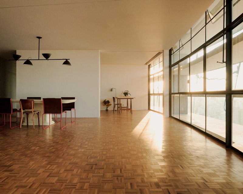 Dining area with herringbone parquet flooring bathed in afternoon sunlight from tall steel-framed windows