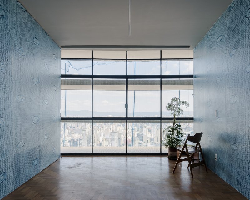 Room with blue mosaic tile walls facing floor-to-ceiling glazing overlooking a dense cityscape