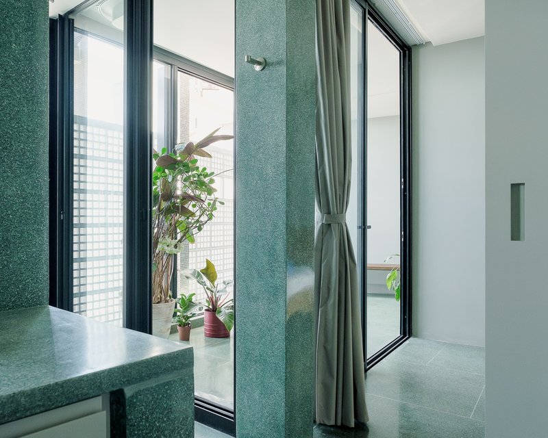 Bathroom corner with green terrazzo wall panels and black-framed windows opening to a planted balcony