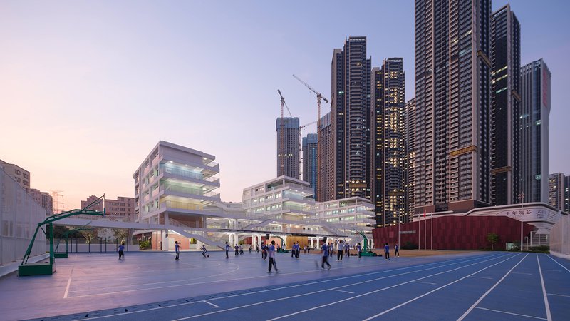 Wide view of the school campus with illuminated facades and students on the sports court at twilight