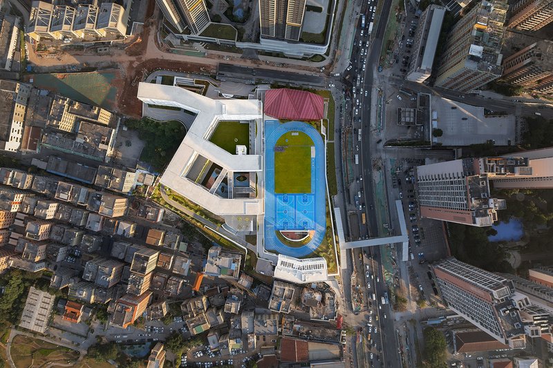 Drone view of the terraced white volumes with rooftop running track and green playing fields in dense urban fabric