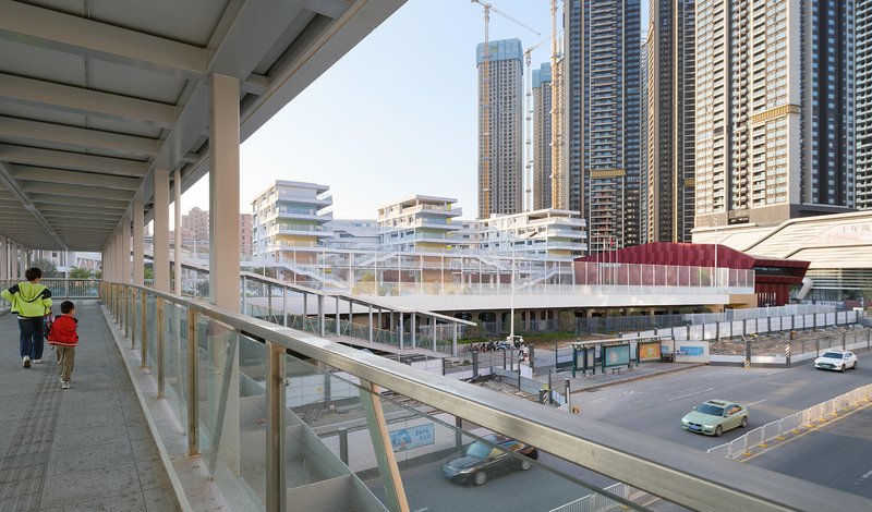 Pedestrian bridge with glazed barrier overlooking the layered white school complex and street below in daylight