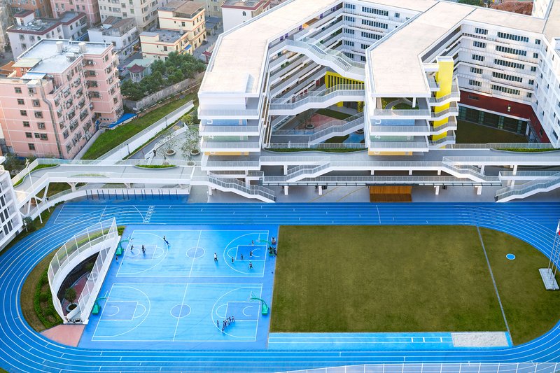 Aerial view of rooftop running track surrounding blue basketball courts and green playing field