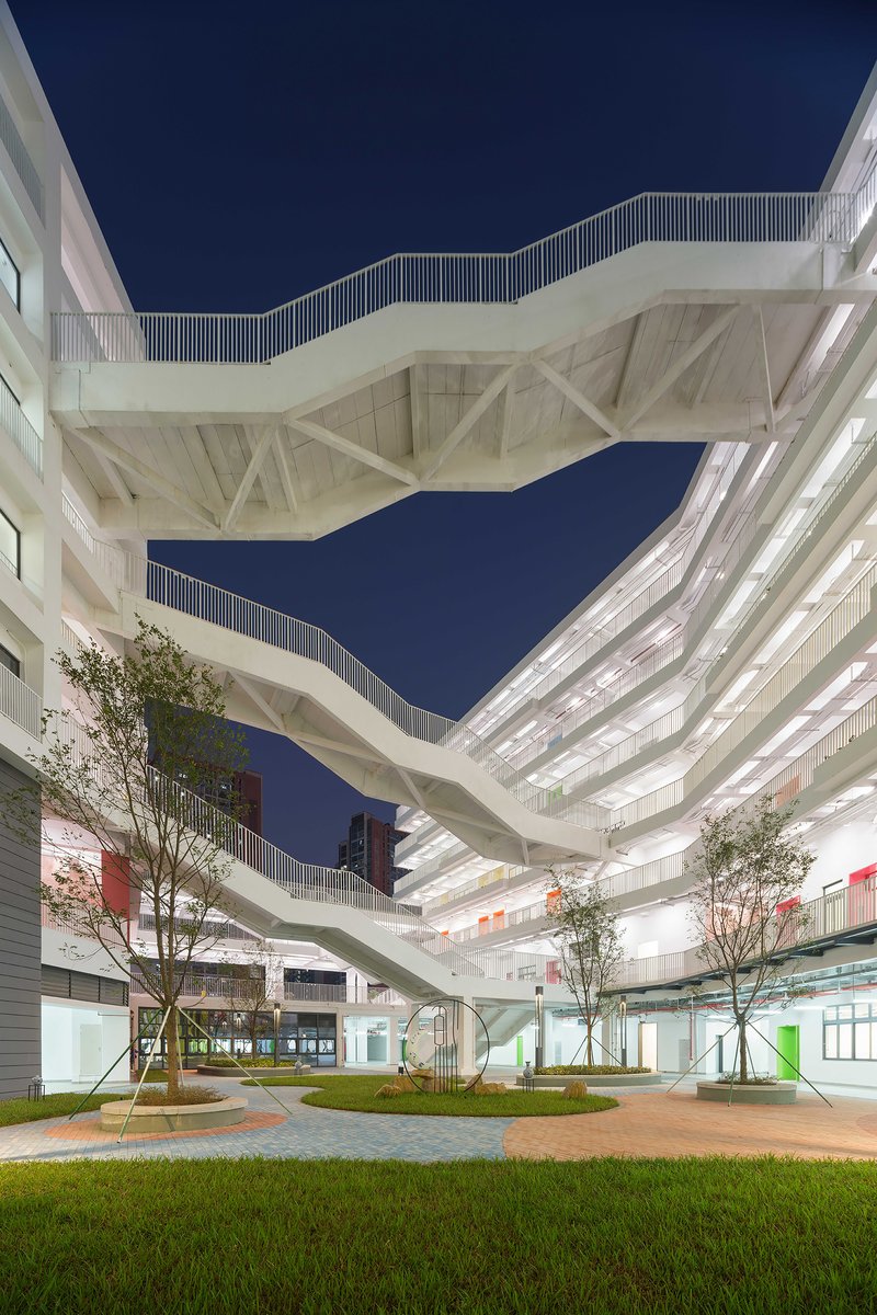 Elevated pedestrian bridges with triangular truss structure connecting buildings across a planted courtyard at dusk
