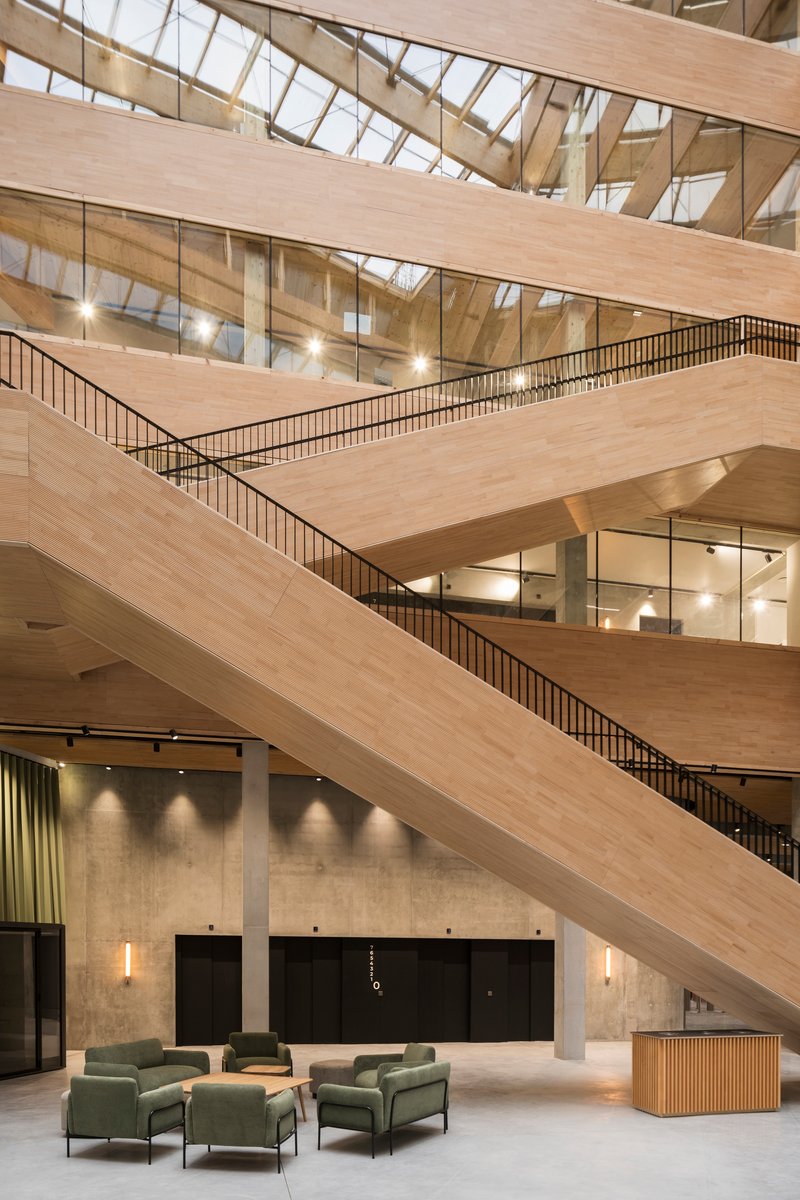 Interior atrium with stacked timber-clad balconies and metal railings under a glazed skylight