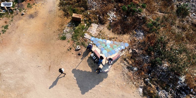 Aerial view of a gathering shelter with multicolored circular roof panels on cleared ground