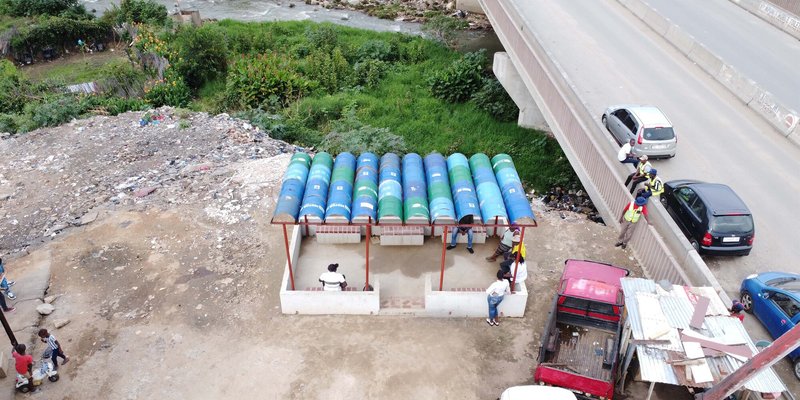 Drone view of the pavilion showing blue and green vaulted canopy beside a highway retaining wall