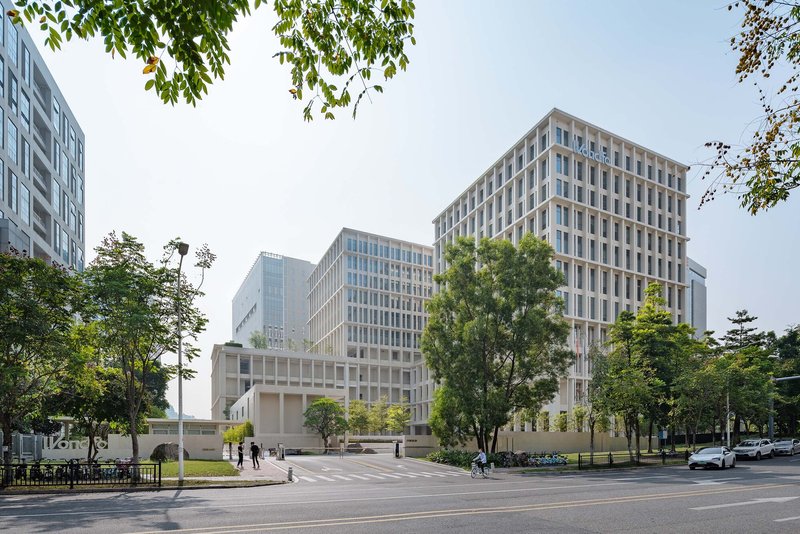Street view of three gridded office tower volumes framed by mature trees and a pedestrian crossing