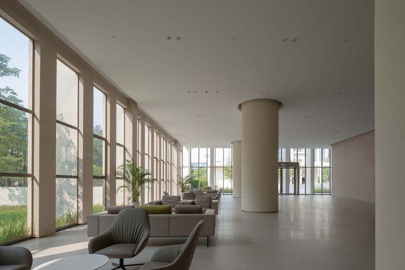 Lobby interior with tall floor-to-ceiling windows, cylindrical column and scattered lounge seating under soft daylight