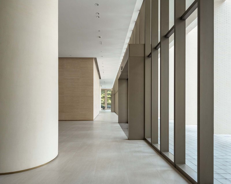 Lobby corridor with curved white column, bronze metal screens and pale stone flooring