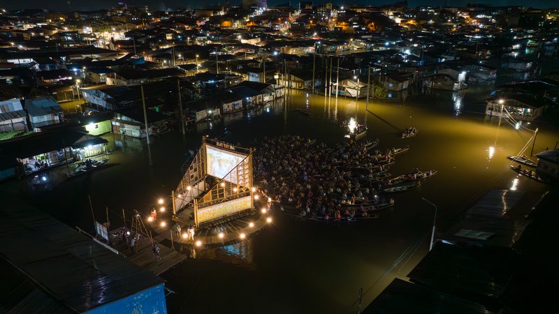 Night aerial view of the illuminated floating pavilion with gathered boats in floodwater