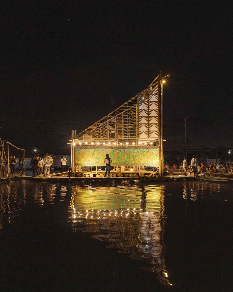 Floating platform with angled bamboo frame and glowing screen reflected in calm water at night